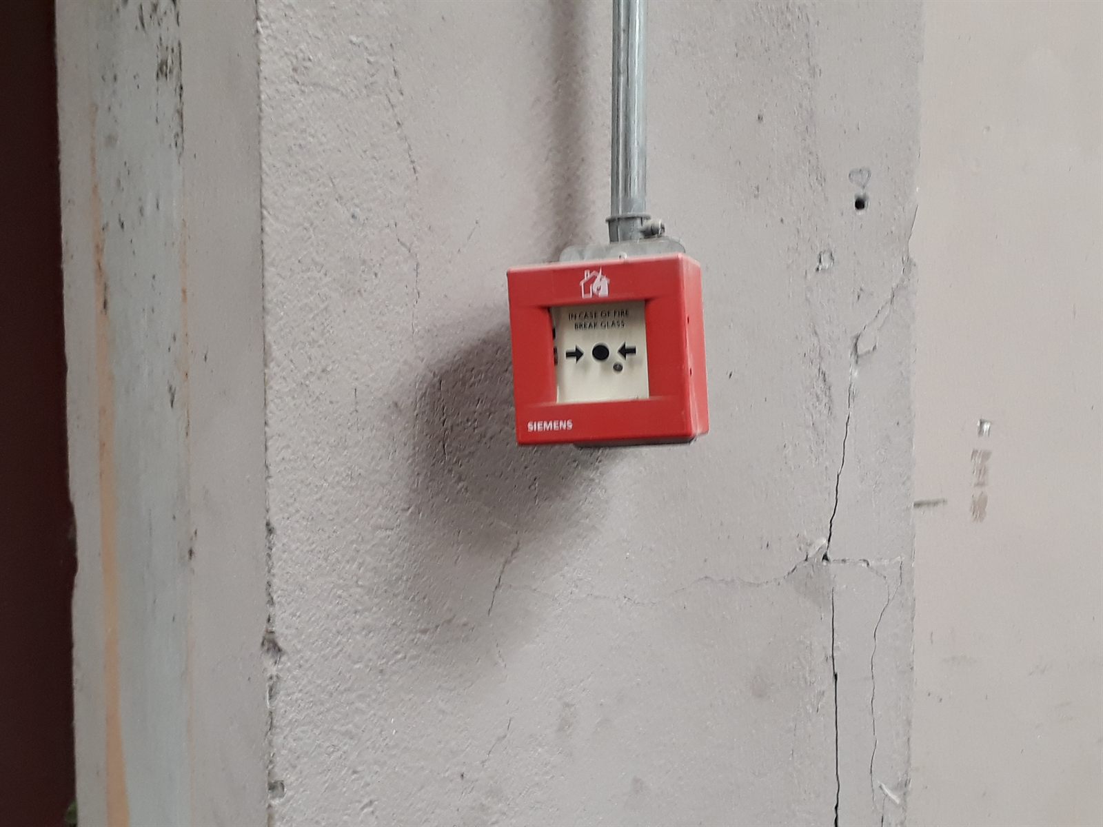 Estación manual de alarma Siemens (pulsador rompe-vidrio) con bajada de cañería conduit EMT a la vista, montaje en pilar de bodega.